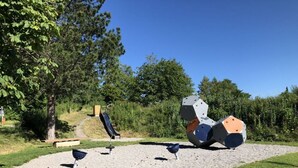 An outdoor sculpture garden with abstract metal structures, a small slide, and a gravel area. - Family Apartment Bavaria (Fuessen)