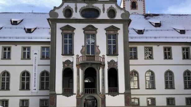 A historic building with a central entrance, symmetrical windows, and a tower in the background. - Family Apartment Bavaria (Fuessen)