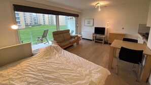 A modern hotel room with a large bed, a desk, a TV, and a balcony with a view of the city. - Apartment in Nieuwpoort With sea View (Nieuwpoort)