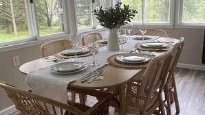 A dining area with a round table set for six, surrounded by wicker chairs.