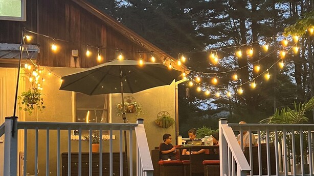 A wooden deck with string lights, a covered seating area, and a stone wall.