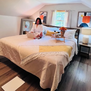 A bedroom with a bed, a laptop, a vase with flowers, and a bedside table with a lamp.