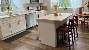 A modern kitchen with white cabinetry, a central island, pendant lighting, and a view of the outdoors through large windows.