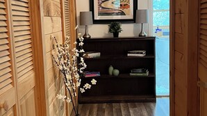 A hallway with wooden paneling, a framed artwork on the wall, a small table with a lamp, and a potted plant.