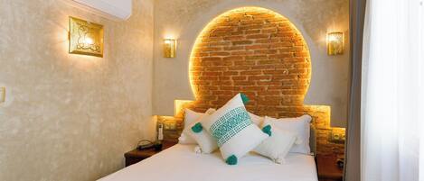 A hotel room with a brick wall arch, a white bed with green and white pillows, and two wall-mounted lamps.