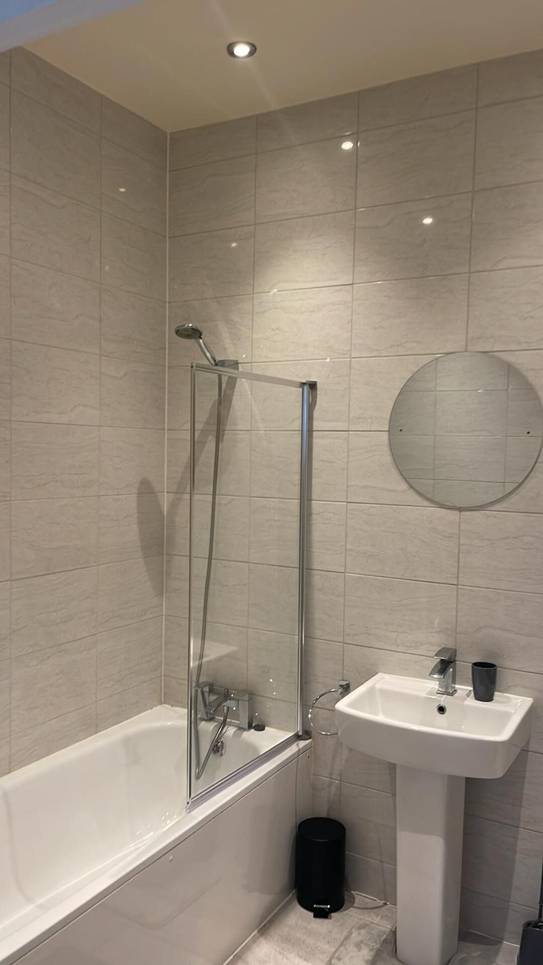 A modern bathroom with a glass-enclosed shower, a white bathtub, and a pedestal sink.
