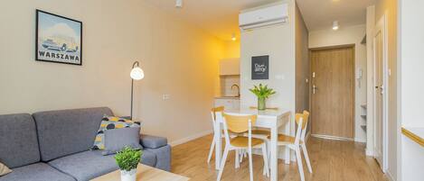 A modern living room with a sofa, a dining table with chairs, a floor lamp, and a small plant.