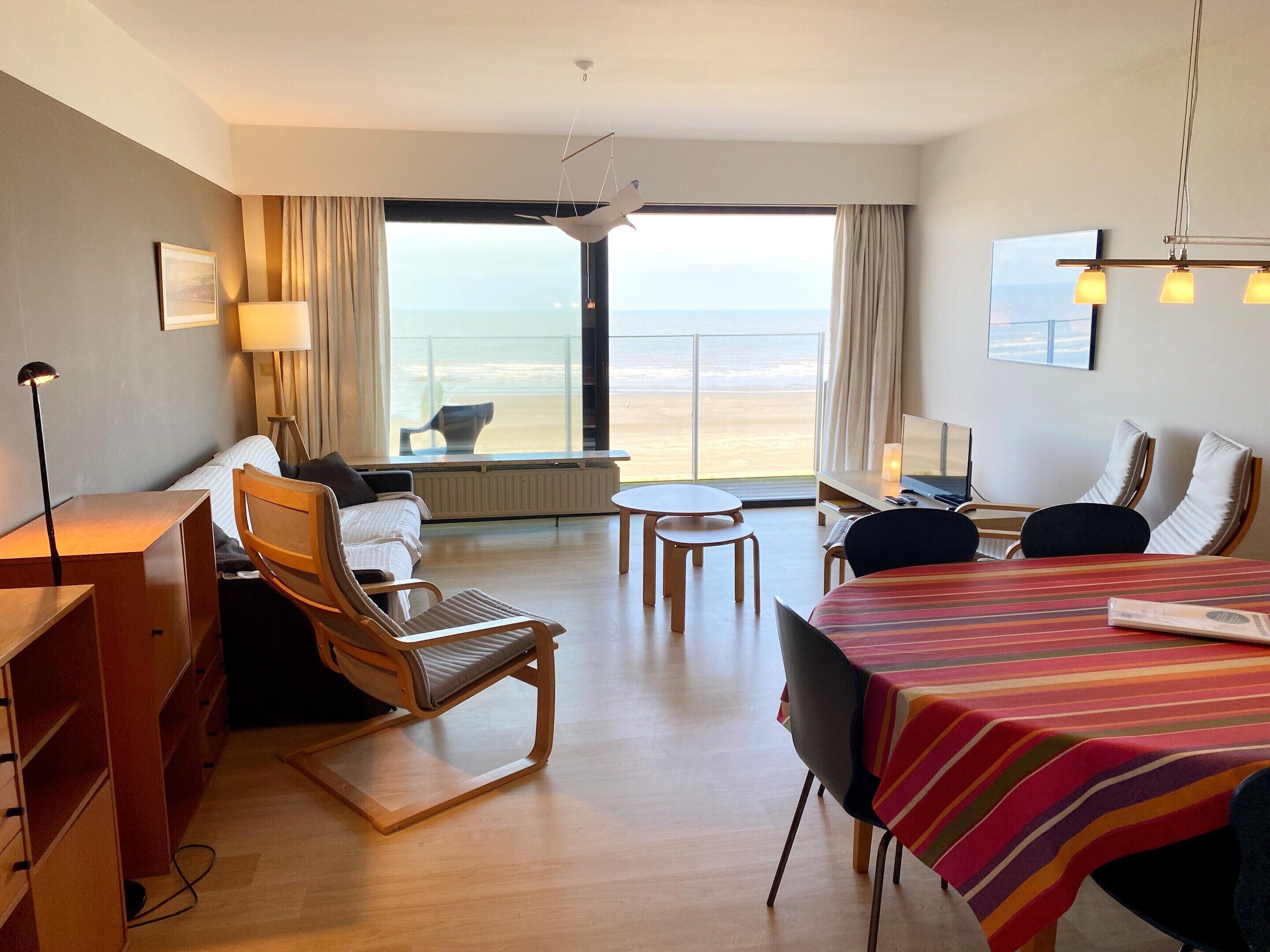 A hotel room with a bed, a desk, a chair, a table, and a view of the beach.