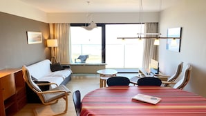 A hotel room with a bed, a desk, a dining table with chairs, a sofa, and a balcony with a view. - Apartment in Nieuwpoort by the Beach (Nieuwpoort)