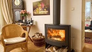 A cozy living room with a wood-burning stove, wicker chair, wooden table, clock, and artwork. - Landhuis Appartement Feldberg Uitzicht (Sankt Maergen)