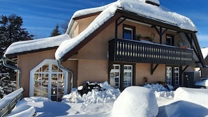 A chalet with a sloped roof covered in snow, a balcony with a railing, and a door with a glass panel. - Landhuis Appartement Feldberg Uitzicht (Sankt Maergen)