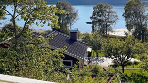 Un quartier résidentiel où se trouve une maison dotée d’un toit en pente, entourée d’une végétation luxuriante et offrant une vue sur un lac.