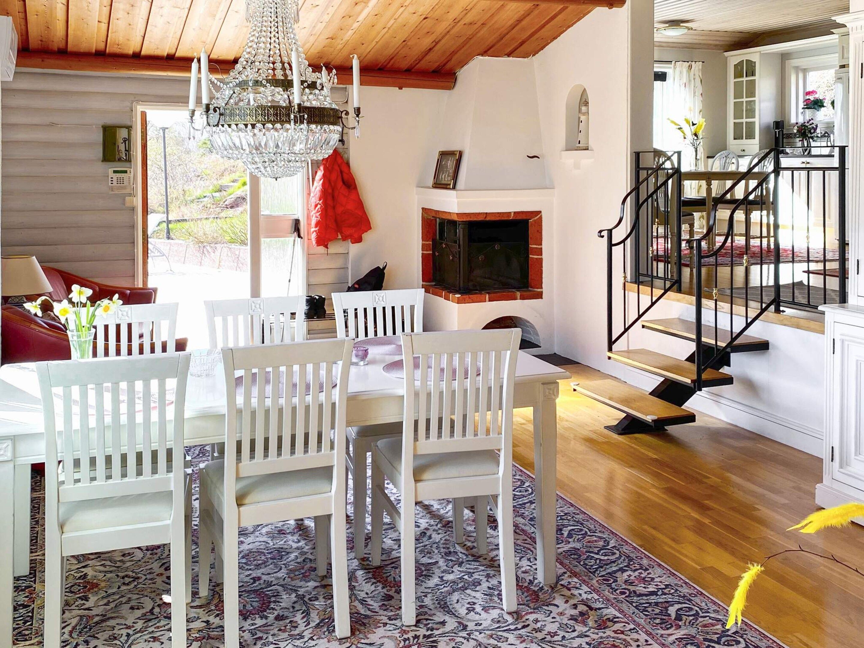 A dining area with a chandelier, white chairs, a table, and a patterned rug.