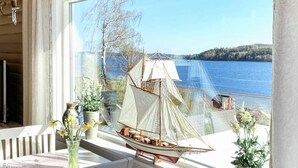 Een kamer met uitzicht op een meer, een model zeilboot en potplanten op een vensterbank.