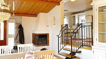 A dining area with a wooden ceiling, a fireplace, and a staircase with black railings.