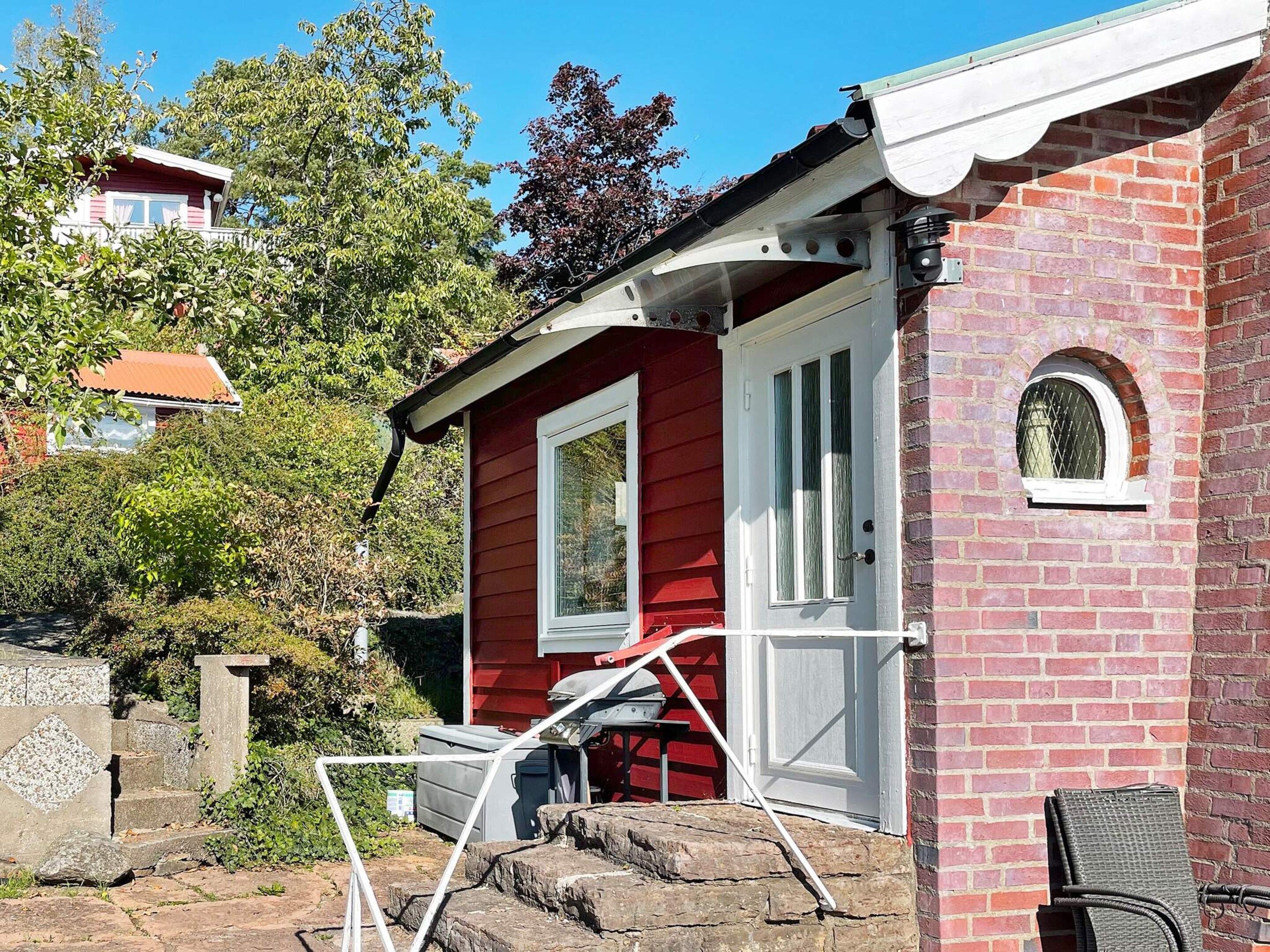 A red brick house with a white door and window, a small porch, and a stone wall.