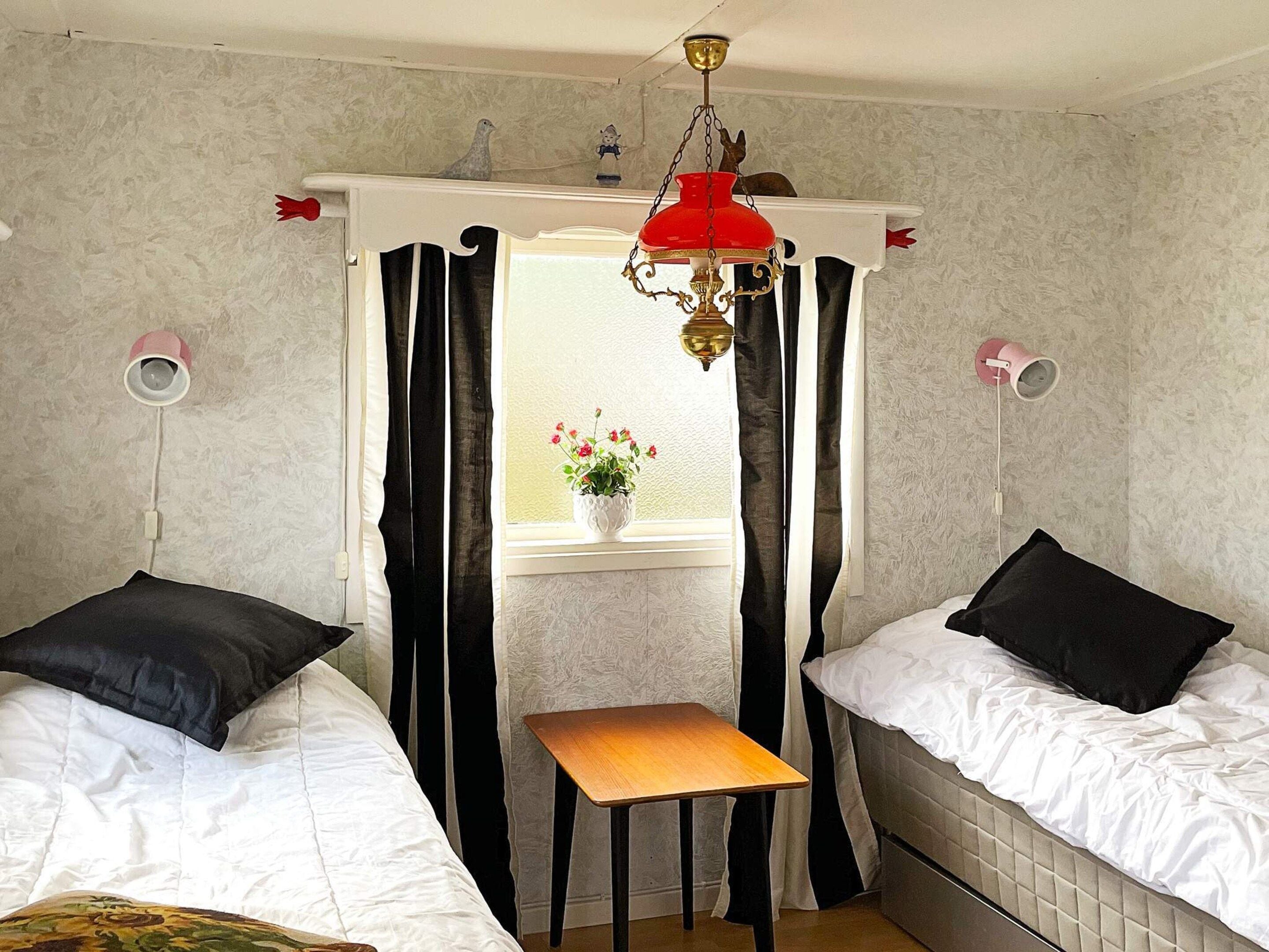 A bedroom with two beds, a small table, and a window with curtains.