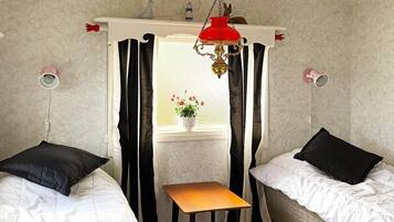 A bedroom with two beds, a small table, and a window with curtains.