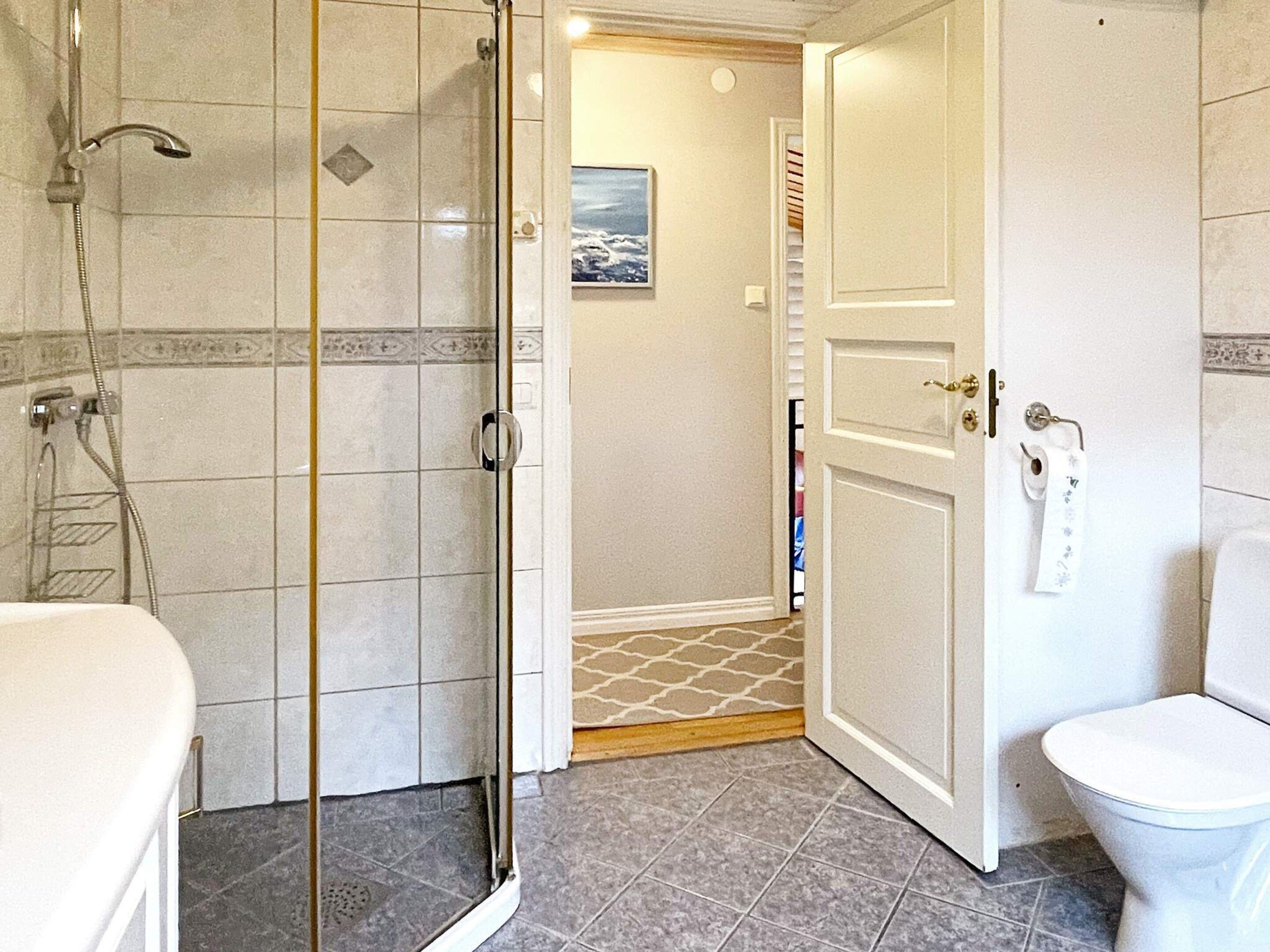 A bathroom with a shower, toilet, and a door leading to another room.