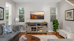 A modern living room with a grey sofa, a wooden coffee table, and a TV on a wooden cabinet. - Asheville`s 5 Star Club!  We Invite You To See What All The Fuss Is About! (Asheville)