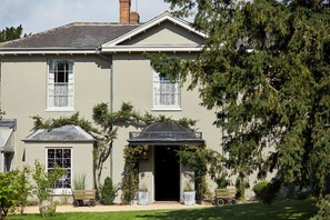 A two-story house with a symmetrical facade, a central entrance with a dark roof, and a small attached structure with a window. - THE PIG in the South Downs - West Sussex (Arundel)