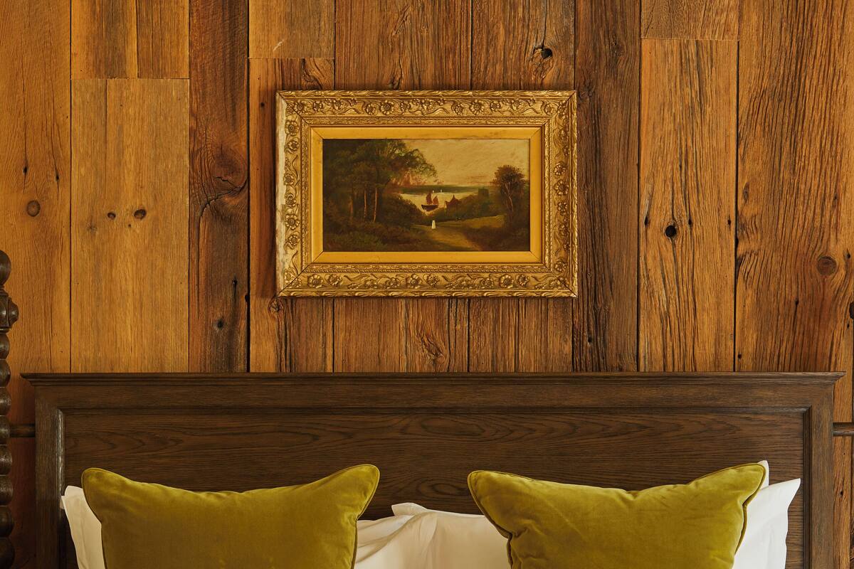 A bed with a tufted headboard, two green pillows, and a framed picture above it.