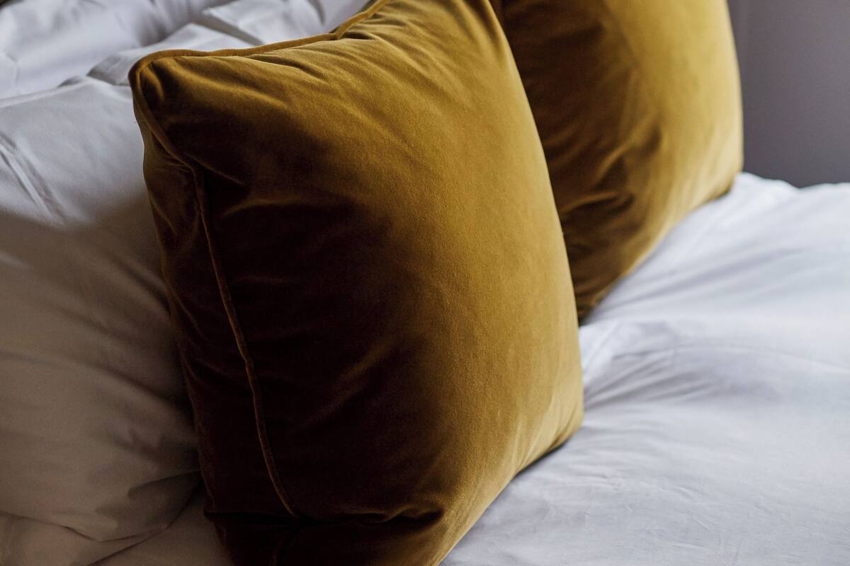 A bed with white linens and two mustard-colored pillows.