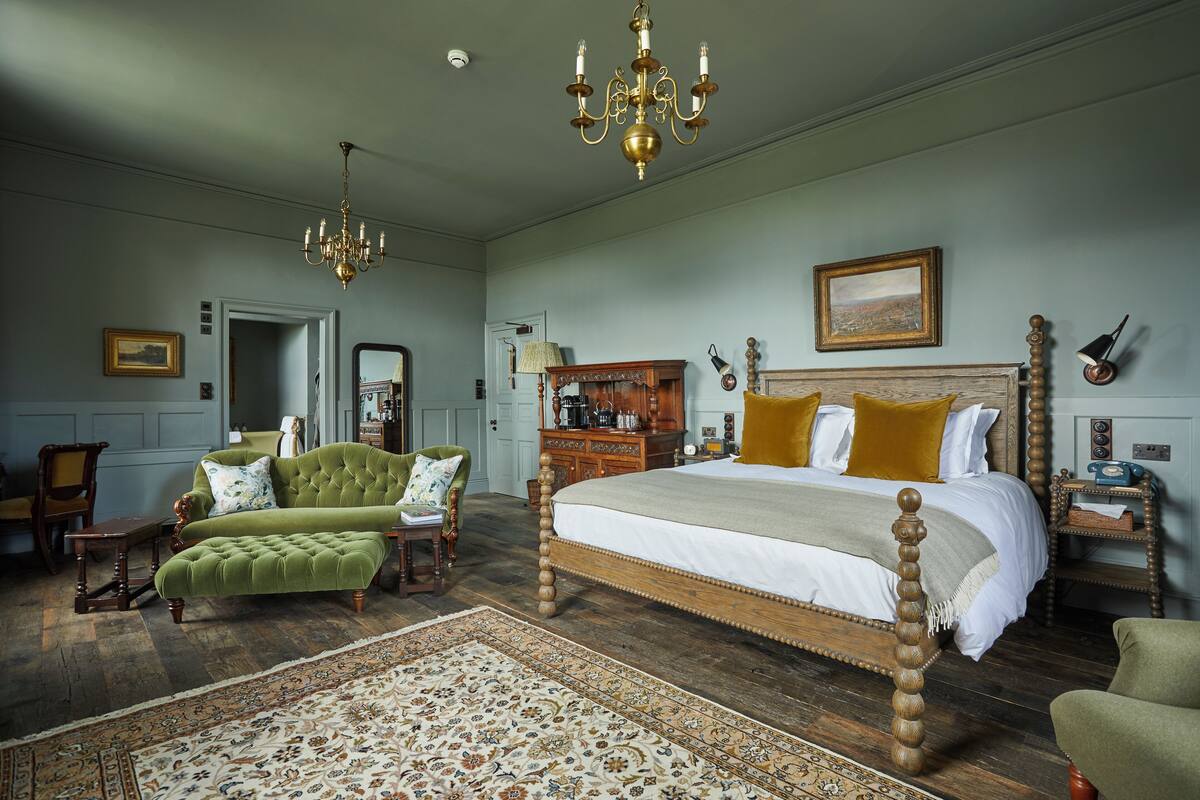 A spacious bedroom with a large bed, a green sofa, a wooden dresser, and a chandelier.