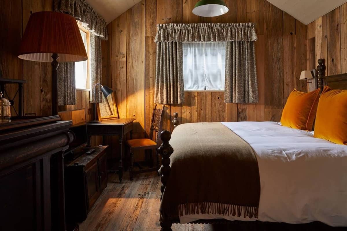 A rustic wooden room with a bed, a desk, and a lamp.