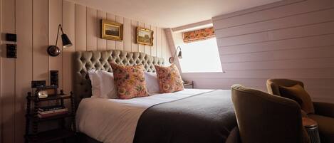 A bedroom with a tufted headboard, floral pillows, a bedside table with books, and a nightstand.