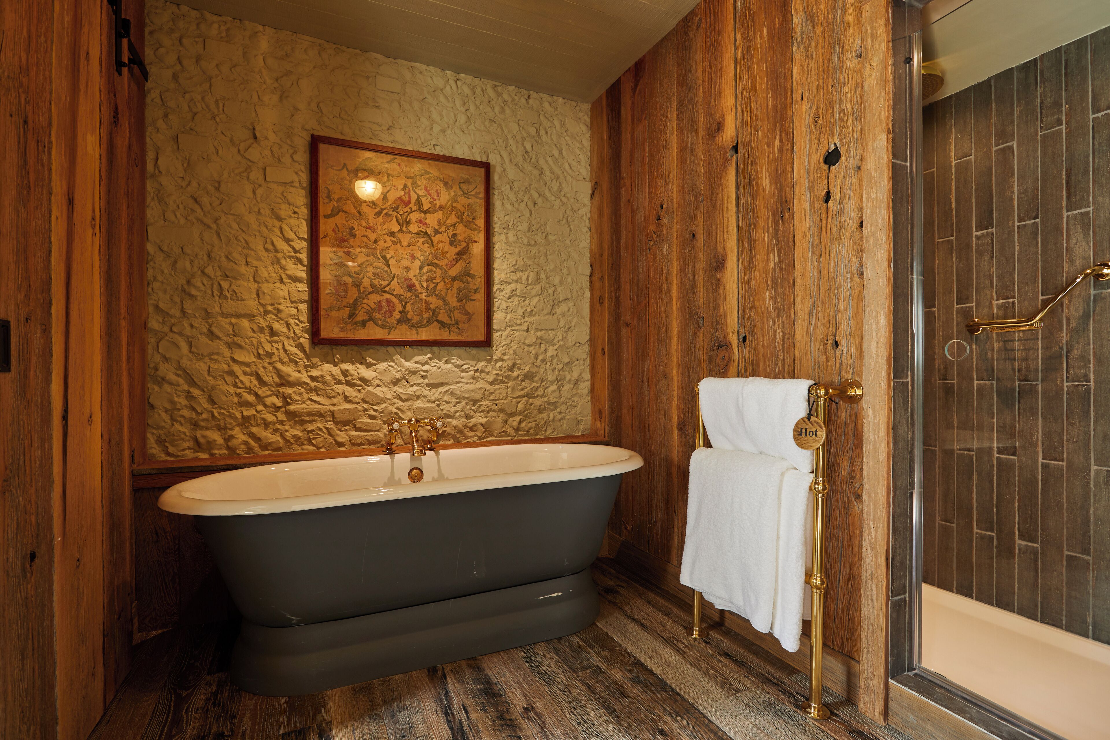 A bathroom with a freestanding bathtub, a wooden wall, and a framed artwork above the tub.