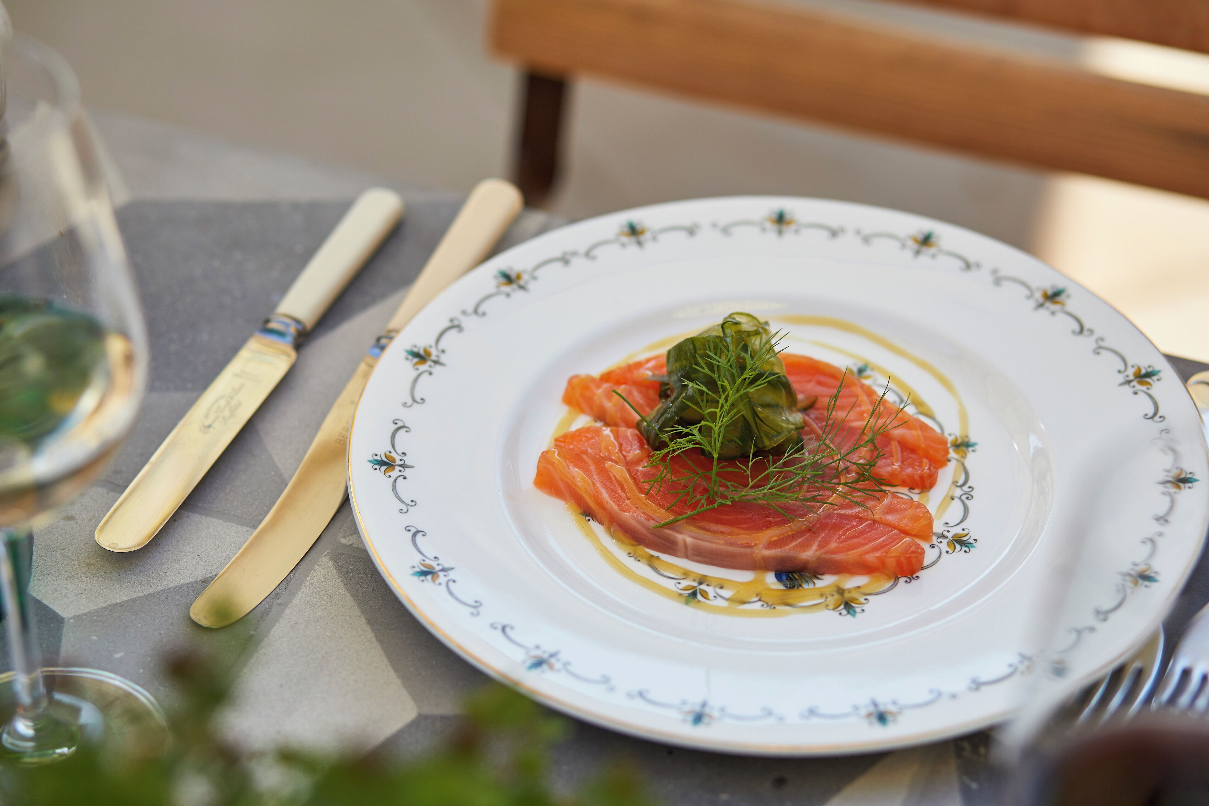 A plate of food with salmon and a garnish, placed on a table with a glass of wine and cutlery.