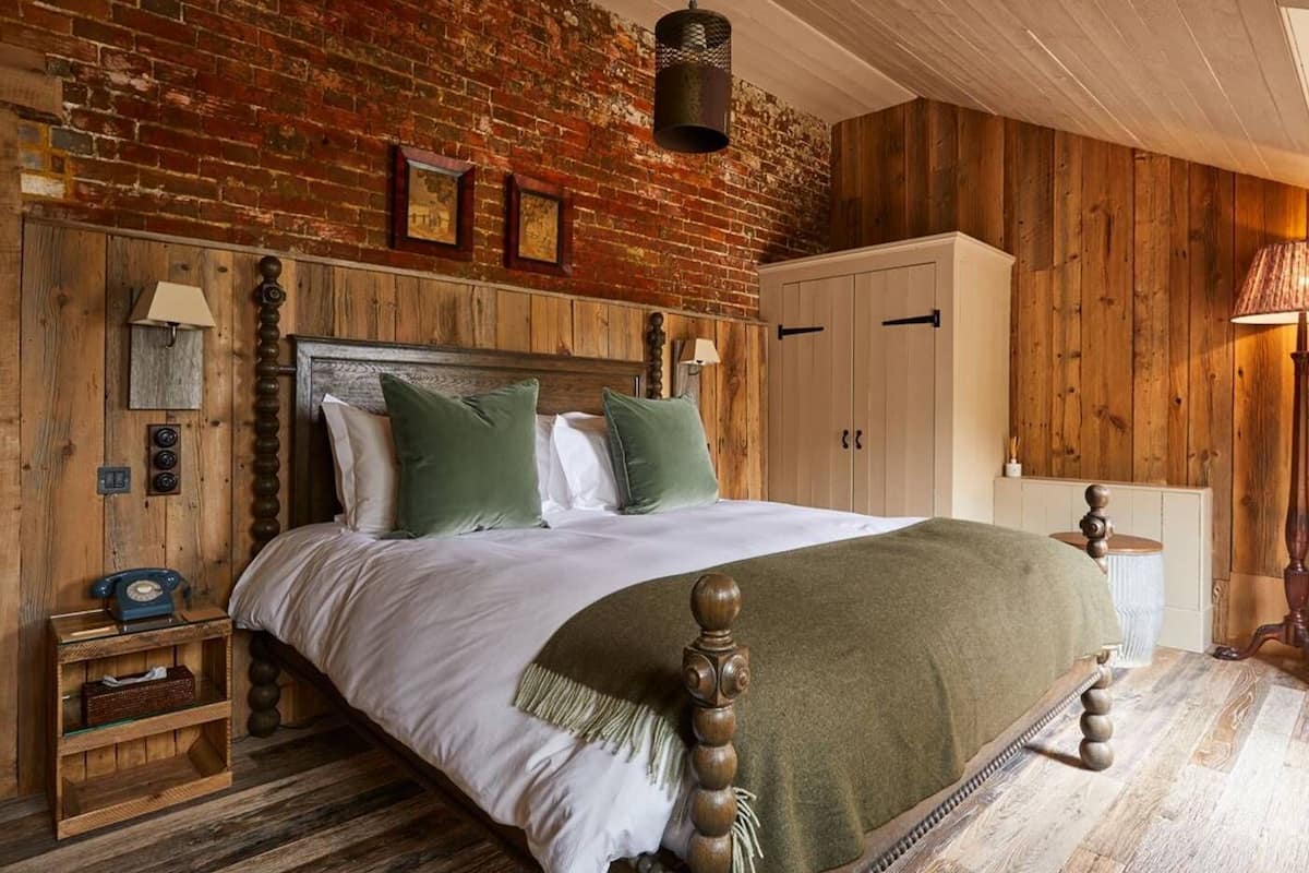 A rustic bedroom with a brick wall, wooden headboard, and a bed with green pillows.
