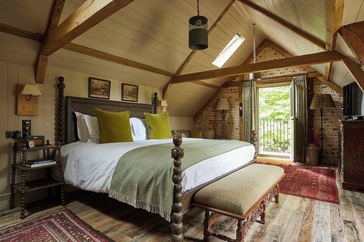 A traditional bedroom with a wooden four-poster bed, a bench, and a view of the outdoors through a window.