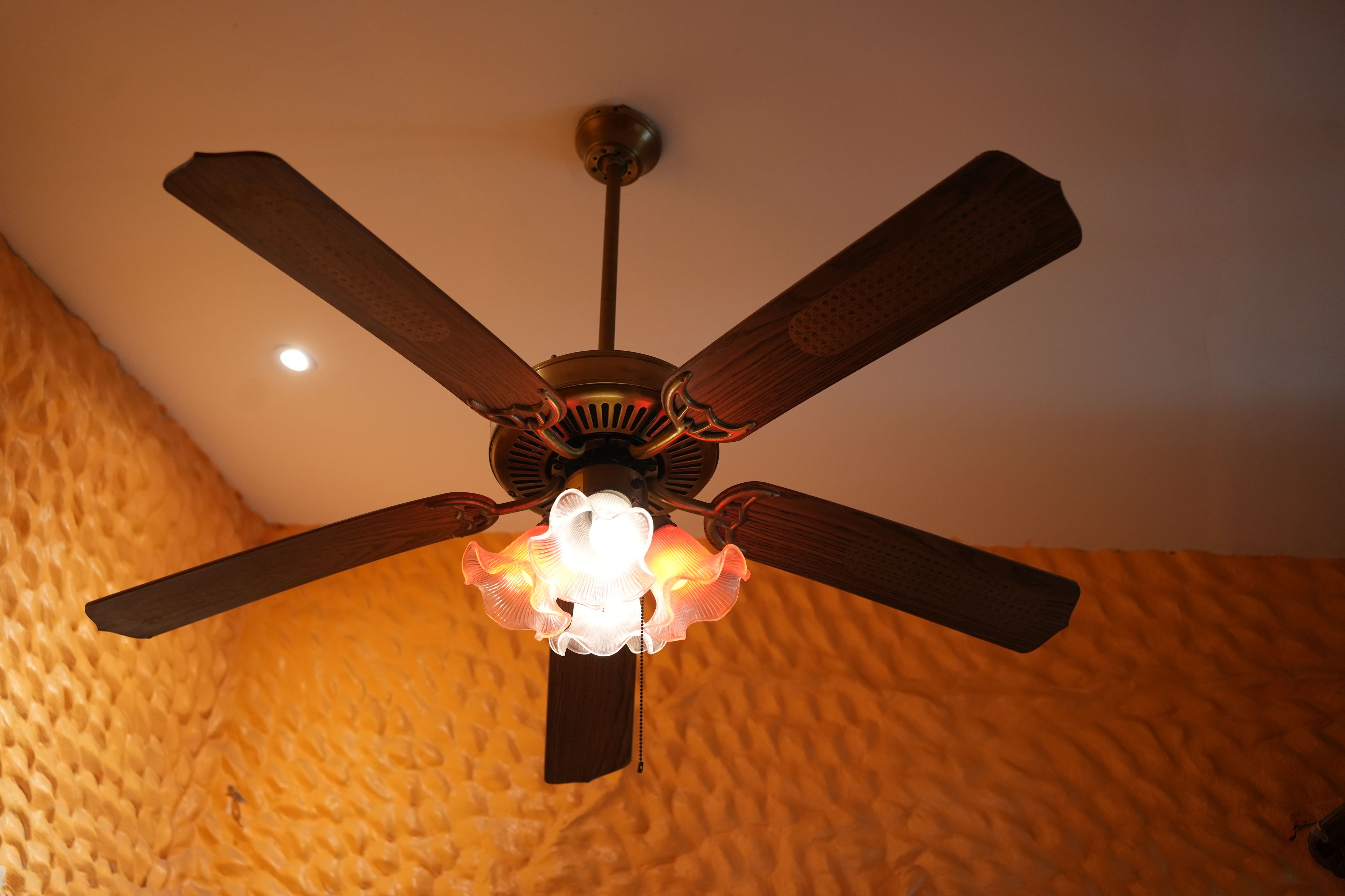 Um ventilador de teto com luminária em um quarto com paredes texturizadas.