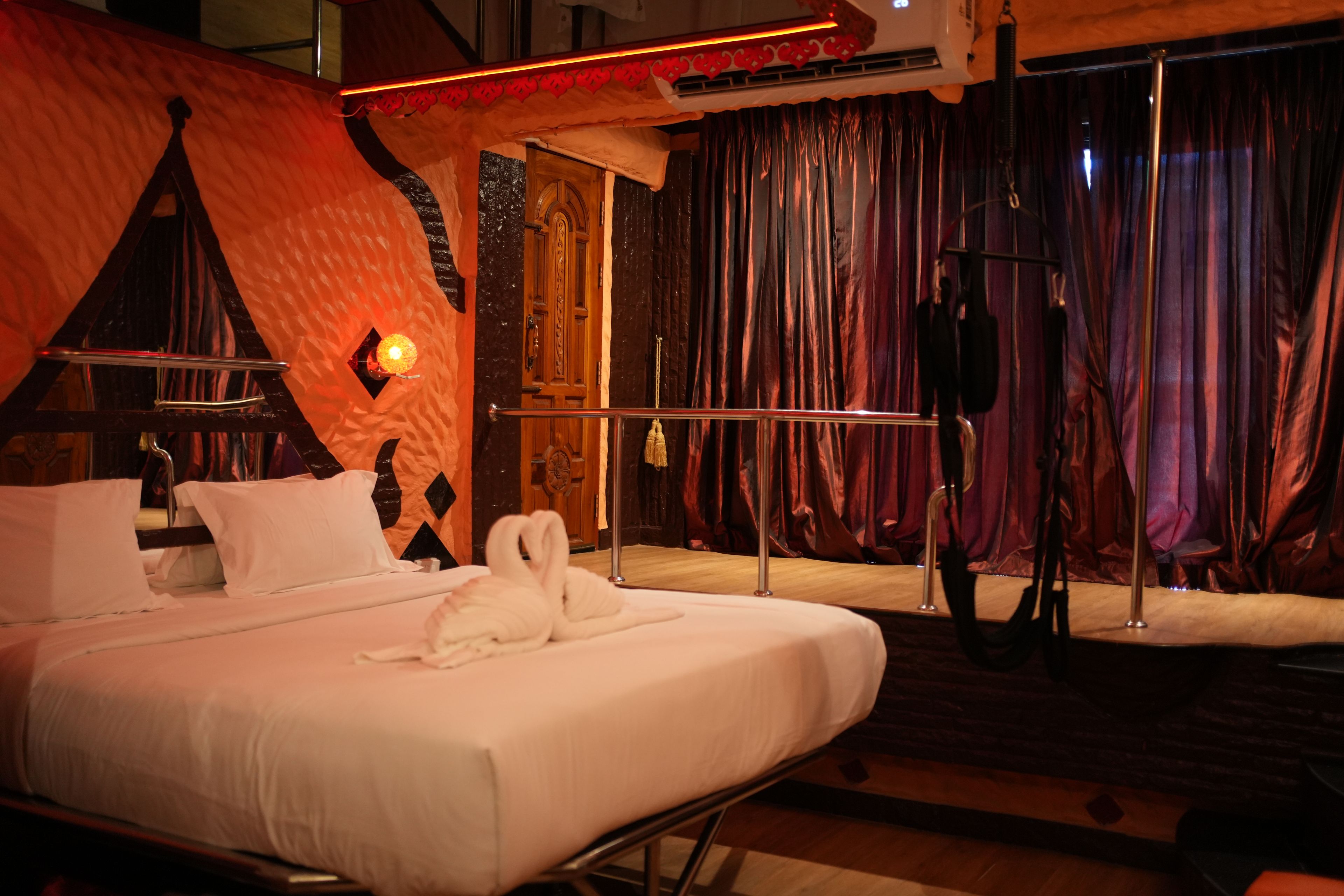 A hotel room with a bed, a mirror, a window with curtains, and a wall-mounted air conditioning unit.