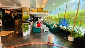 Una hall d'albergo moderna con divani verdi, una televisione e ampie finestre.