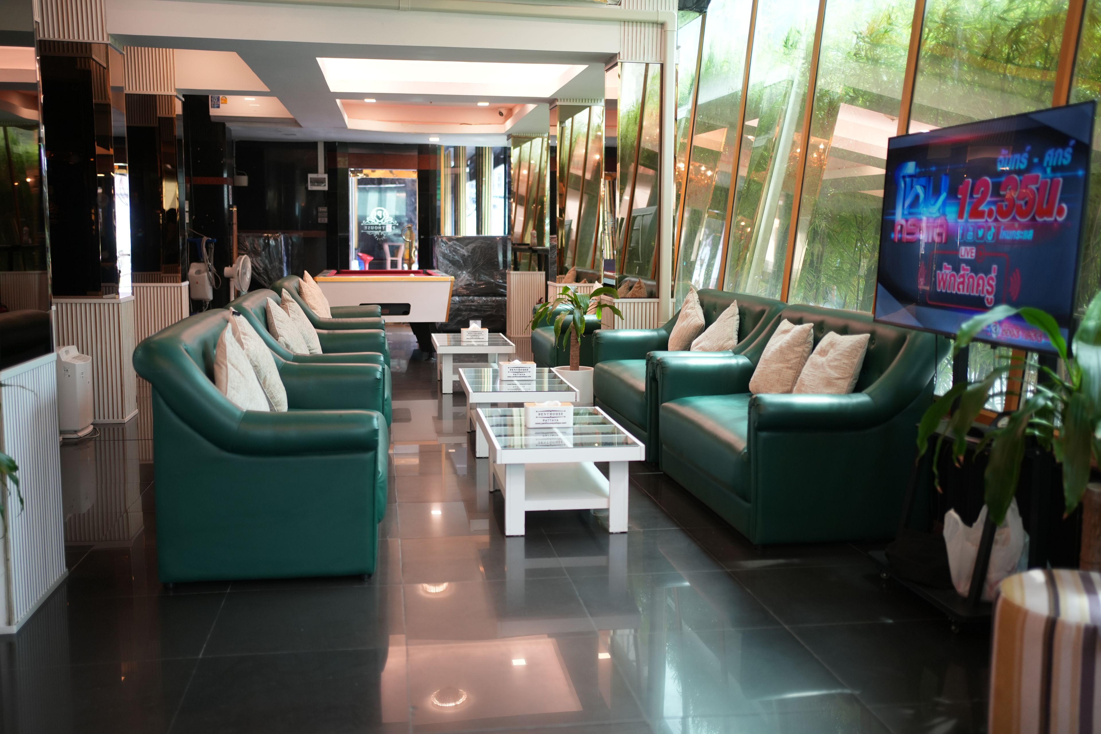 A modern lobby with green sofas, a reception desk, and a TV displaying a program.