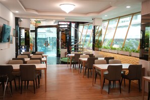 A restaurant with multiple tables and chairs, a glass door entrance, and a view of the outside through large windows. - Penthouse Pattaya (Pattaya)