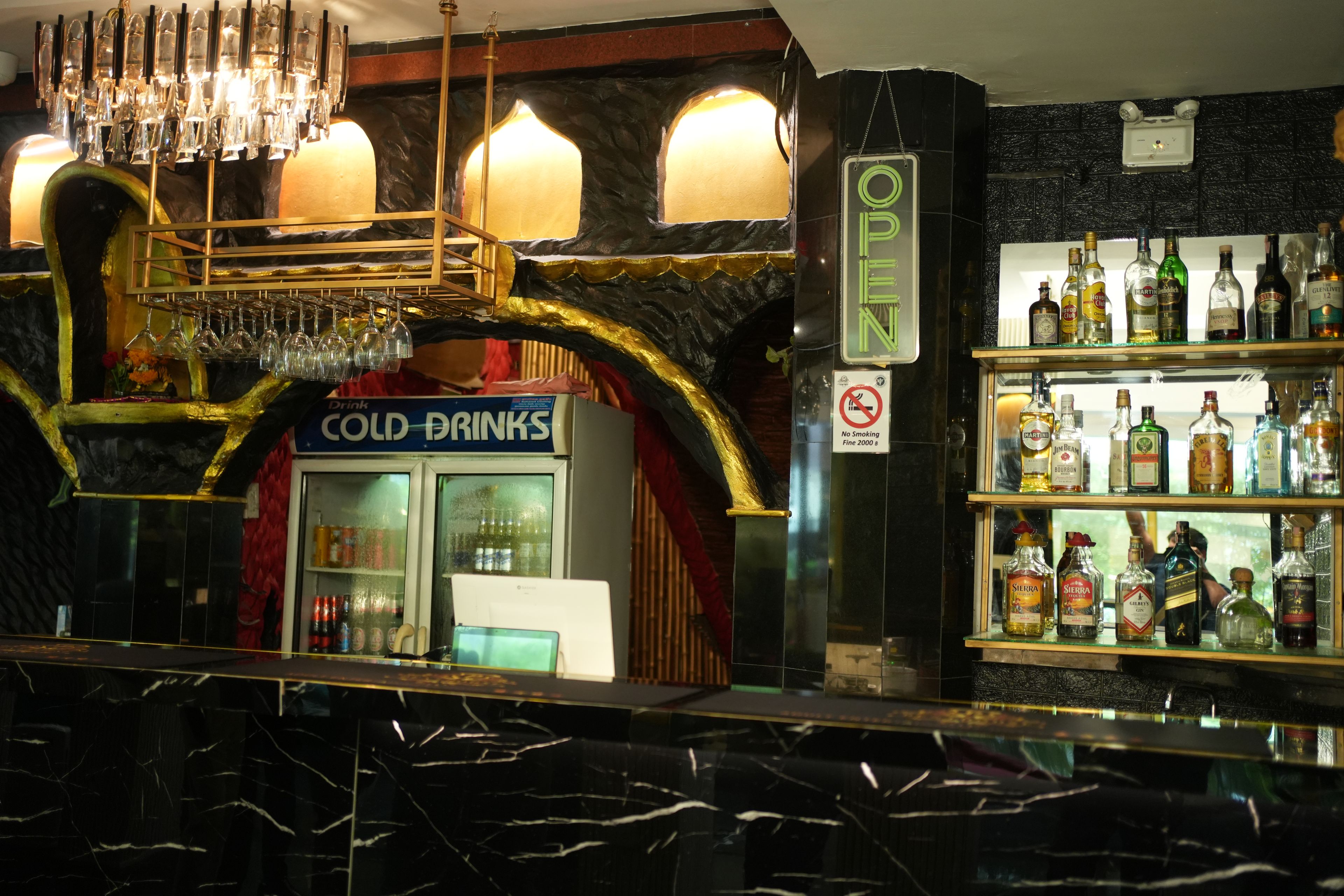 Zona de bar con un cartel que dice 'COLD DRINKS', un cartel de 'NO SMOKING' y estantes llenos de diferentes botellas de licor.