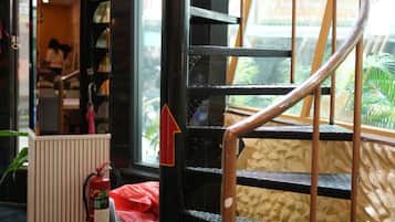 Una escalera de caracol con barandilla de metal, un extintor y una señal roja con forma de flecha en un poste.