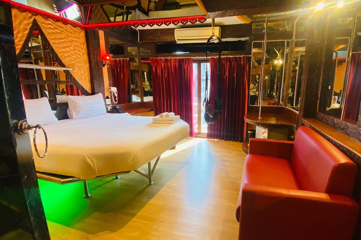 A hotel room with a bed, a red sofa, a mirror, and a wooden floor.