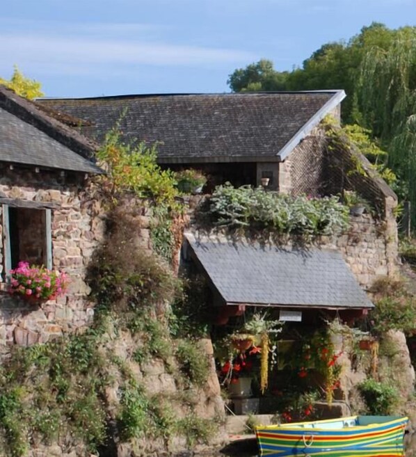 A stone building with a sloped roof, a small attached structure, and a boat in front.