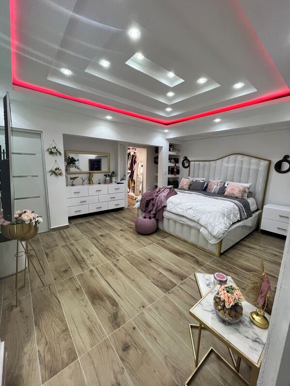 Ein modernes Schlafzimmer mit Bett, Nachttischen, Schminktisch und begehbarem Kleiderschrank.