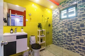 Ein Badezimmer mit gelben Wand, weißem Waschbecken, Toilette, Dusche und Spiegel.