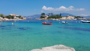 A coastal scene with clear turquoise waters, boats, and buildings along the shore. - Charm and tranquility, panoramic views of the sea and the islands, 3 minutes from the beaches (porticcio)
