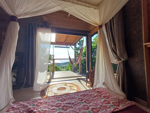 A room with a bed, a view of the outdoors, and a window with curtains.
