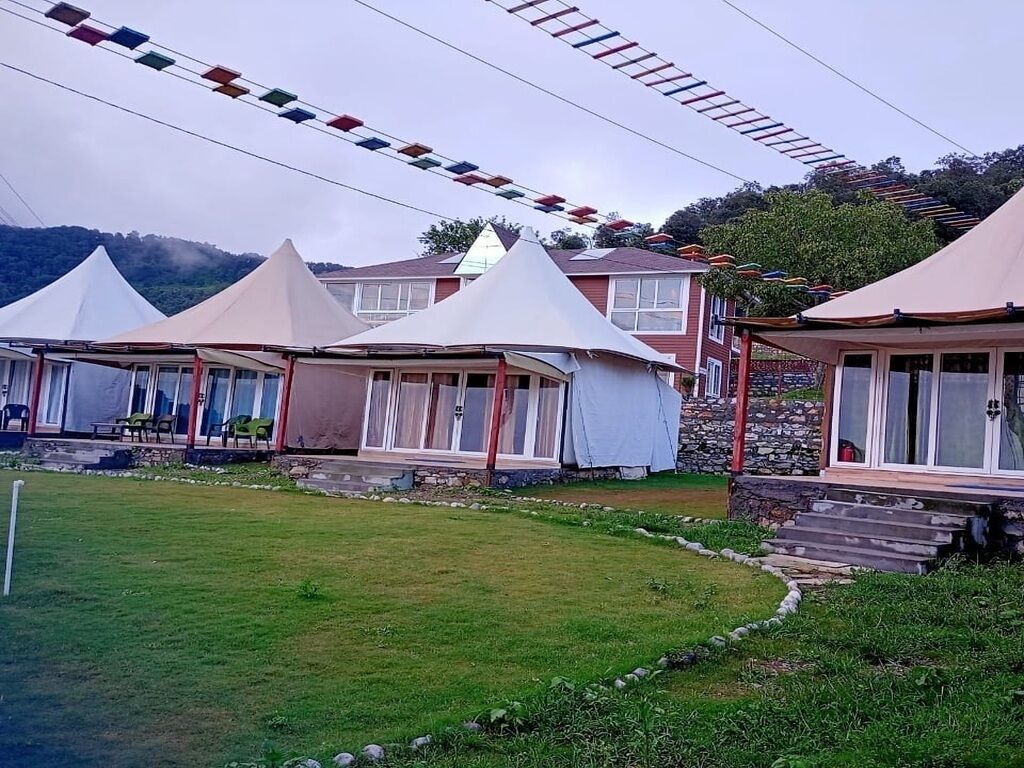 Una hilera de carpas blancas con fachada de piedra, ubicadas en una zona cubierta de césped bajo un cielo despejado.