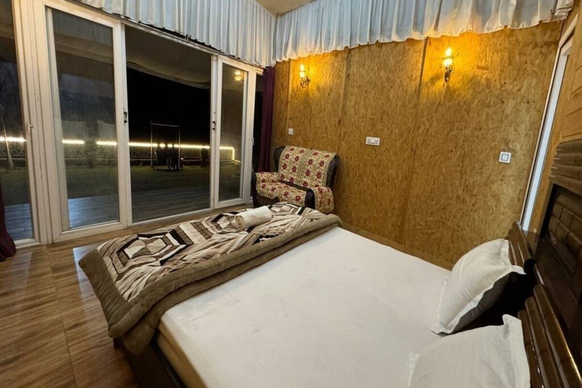 A bedroom with a bed, a chair, a wooden wall, and a sliding glass door leading to an outdoor area.