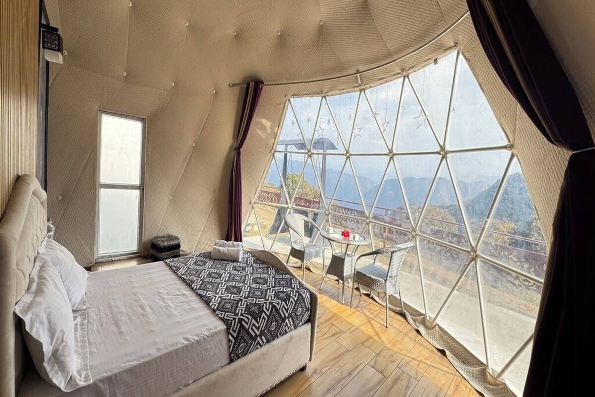 A bedroom with a large window, a bed, and a seating area with a view of the mountains.